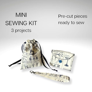 May include: A mini sewing kit with three projects featuring pre-cut pieces ready to sew. The set includes a drawstring pouch, a small envelope-style wallet with a blue button, and a wrist strap, all made from cream fabric with a blue vintage sewing print.