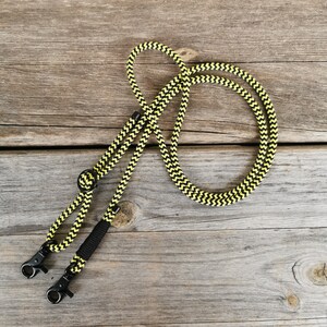 Könnte beinhalten: Eine schwarze und gelbe gemusterte Seil-Leine mit zwei Metall-Clips.