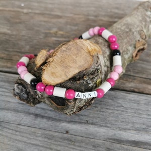 May include: A pink and white beaded bracelet with black beads and the name "ANNI" spelled out in white letters.