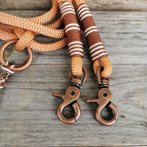 May include: Two brown and white striped dog leashes with copper-colored clasps. The leashes are made of rope and have a paw print charm.