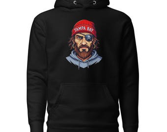 Pode incluir: Moletom preto com capuz com um gráfico de um pirata com um gorro vermelho que diz "TAMPA BAY". O pirata tem um tapa-olho e uma longa barba. O moletom tem um bolso frontal e um capuz com cordão.