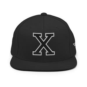 Può includere: Cappellino da baseball nero a tinta unita con una grande lettera X nera con contorno bianco ricamata sul davanti.