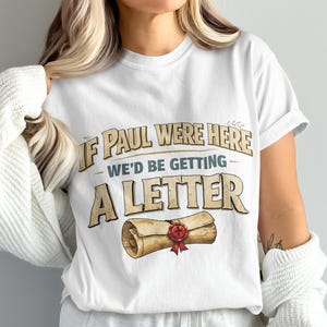 White t-shirt with text "IF PAUL WERE HERE WE'D BE GETTING A LETTER" and a scroll graphic.