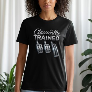Może przedstawiać: Czarny t-shirt z krótkim rękawem z białym napisem Classically TRAINED nad grafiką przedstawiającą trzy metalowe pedały samochodowe, w tym sprzęgło, hamulec i gaz, umieszczone w rzędzie na przodzie ubrania.