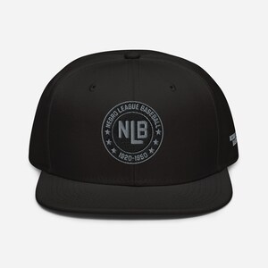 Puede incluir: Gorra de béisbol negra con visera plana, con un emblema bordado gris. El emblema dice "NEGRO LEAGUE BASEBALL", "NLB 1920-1950". La gorra tiene un ajuste estructurado y una visera plana. El texto "NEGRO LEAGUE BASEBALL" también está en el lateral.