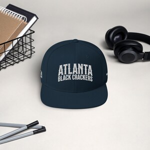 Op de afbeelding: Een donkerblauwe baseballpet met een wit geborduurd logo met de tekst "Atlanta Black Crackers".