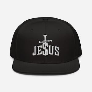 Op de afbeelding: Zwarte baseballpet met een wit geborduurd kruis en het woord "JESUS" op de voorkant.