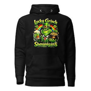 May include: Black hoodie featuring a green Grinch character with a leprechaun hat, holding a beer and a pot of gold. The design includes the text "Lucky Grinch Shenanigans" with a rainbow and shamrocks.