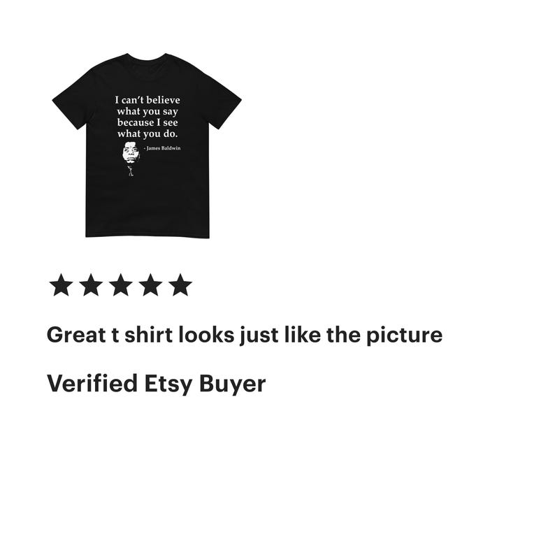 May include: A black short-sleeved t-shirt featuring white text that reads I can't believe what you say because I see what you do, followed by the name James Baldwin and a small black and white portrait of the author.
