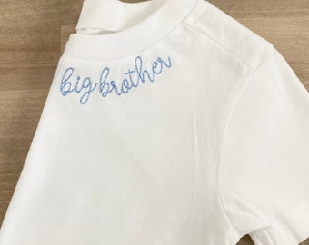 May include: White t-shirt with blue embroidered text that says "big brother".