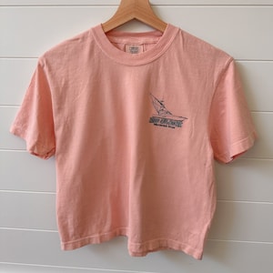 Könnte beinhalten: Ein pfirsichfarbenes T-Shirt mit einer schwarz-weißen Grafik eines Segelboots und dem Text "No Slack" und "Marshall River".