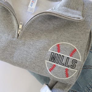 May include: Gray sweatshirt with a zipper and a baseball-themed embroidered patch that says "MILLS" in black lettering.