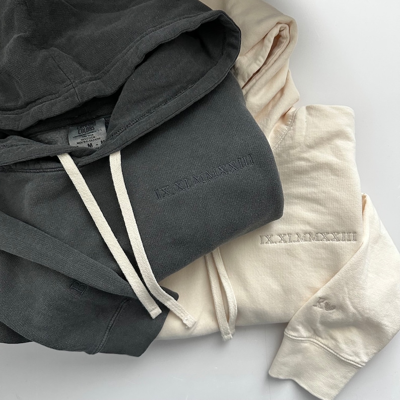 Puede incluir: Dos sudaderas con capucha, una gris oscuro y otra beige claro. La sudadera gris tiene el texto "IX.XI.MMXIII" bordado en la parte delantera. La sudadera beige tiene el texto "IX.XI.MMXIII" bordado en la parte delantera y el texto "Comfort Colors" en la etiqueta.