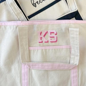Może przedstawiać: Beżowa torba typu tote z r&oacute;żowym wykończeniem i haftowanym r&oacute;żowym monogramem "KS" z przodu.