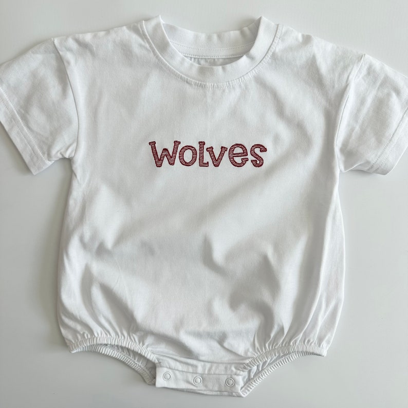 May include: White baby onesie with short sleeves and a red embroidered word "Wolves" on the front.