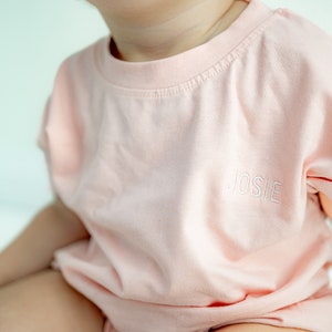 May include: A pale pink t-shirt with short sleeves and the name "JOSIE" embroidered on the front.