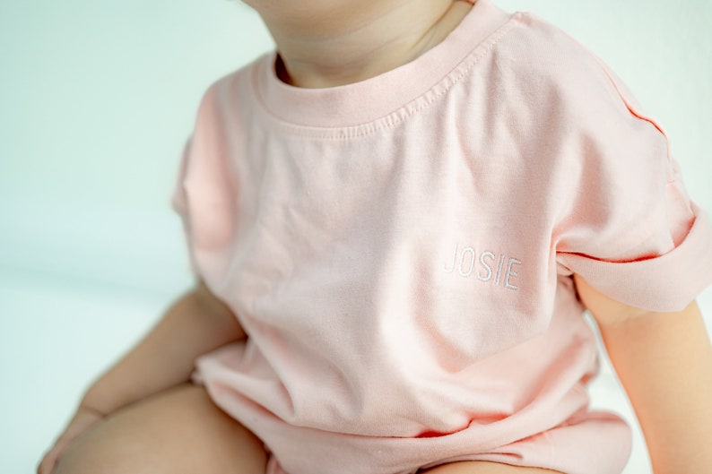 May include: A pale pink t-shirt with short sleeves and the name "JOSIE" embroidered on the front.
