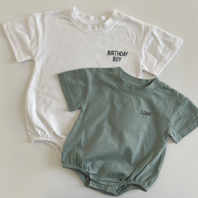 May include: Two baby shirts, one white with the text "Birthday Boy" and one green with the name "Liam" embroidered on the front.