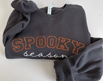 Puede incluir: Una sudadera gris oscuro con el texto "SPOOKY season" bordado en naranja y blanco.