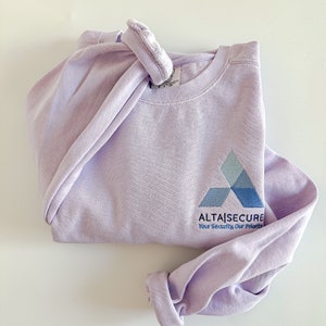 Op de afbeelding: Een lavendelkleurig sweatshirt met een blauw en grijs logo met de tekst "AltaSecure" en "Your Security, Our Priority".