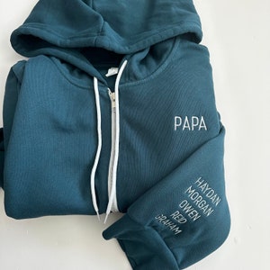 May include: A teal blue zippered hoodie with the word "PAPA" embroidered on the front and the names "HAYDAN, MORGAN, OWEN, REID, GRAHAM" embroidered on the sleeve.