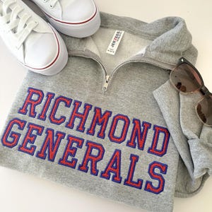 May include: A gray sweatshirt with the words "RICHMOND GENERALS" in red and blue lettering. The sweatshirt has a quarter-zip closure and is paired with white sneakers and sunglasses.