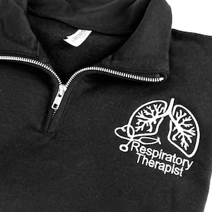 May include: Black quarter-zip sweatshirt with a white embroidered design of a stethoscope and lungs with the text "Respiratory Therapist".