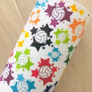 May include: White faux leather with a colorful volleyball and star pattern. The volleyballs are outlined in black and the stars are in various colors including red, orange, yellow, green, blue, and purple.