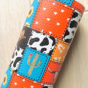 May include: A patchwork fabric with a variety of patterns, including cowhide, stars, sunflowers, and a cactus. The fabric is orange, blue, black, and white.