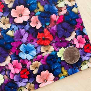 May include: A close-up of a fabric with a floral pattern. The fabric is covered in small, colorful flowers in shades of pink, purple, blue, red, and yellow. A US quarter is placed on the fabric to show the scale.