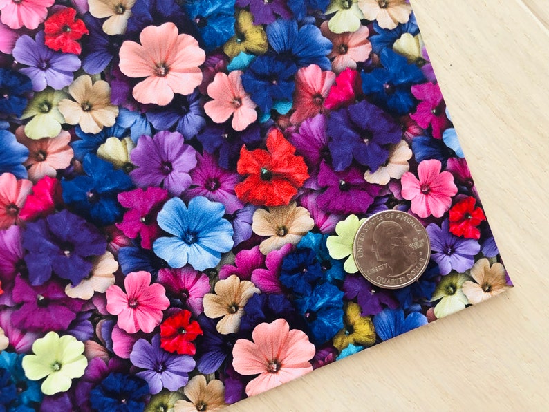 May include: A close-up of a fabric with a floral pattern. The fabric is covered in small, colorful flowers in shades of pink, purple, blue, red, and yellow. A US quarter is placed on the fabric to show the scale.