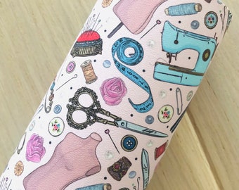 May include: A pink and white fabric with a repeating pattern of sewing-themed illustrations. The pattern includes sewing machines, spools of thread, buttons, scissors, measuring tape, and a dress form.