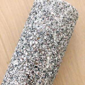May include: Close-up of silver glitter fabric with a fine, sparkly texture. The glitter is a mix of silver and white, creating a shimmering effect.