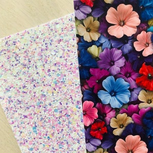 May include: Two sheets of decorative craft paper. One sheet is white with iridescent glitter and the other sheet has a floral pattern with pink, purple, blue, red, and yellow flowers.