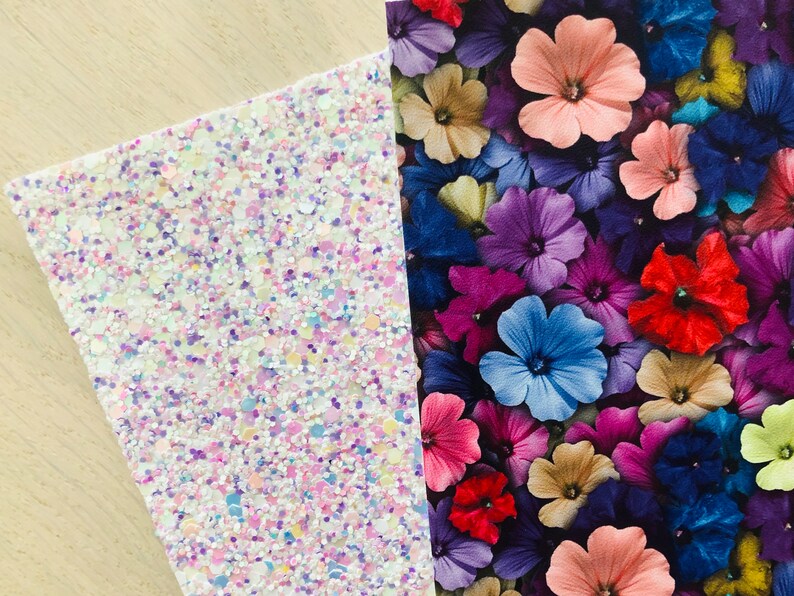 May include: Two sheets of decorative craft paper. One sheet is white with iridescent glitter and the other sheet has a floral pattern with pink, purple, blue, red, and yellow flowers.