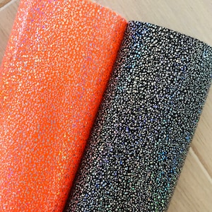 May include: Two sheets of iridescent holographic vinyl with a speckled pattern. One sheet is orange and the other is black.