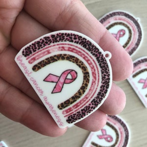 May include: Pink ribbon with a leopard print rainbow design and the text "breast cancer awareness".