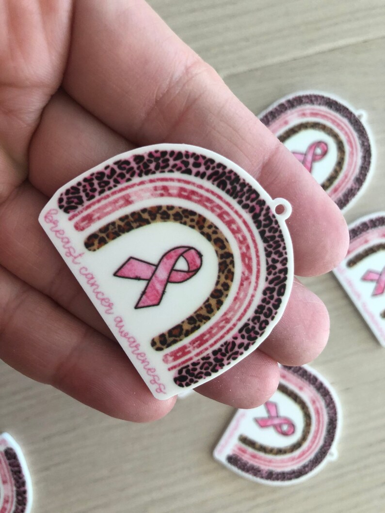 May include: Pink ribbon with a leopard print rainbow design and the text "breast cancer awareness".