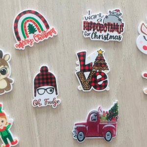 May include: A set of nine Christmas-themed wooden ornaments. The ornaments feature various designs, including a reindeer, a snowman, an elf, a truck, a rainbow, and a hippopotamus. The ornaments are all painted in bright colors and have a festive feel.