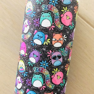 May include: Black faux leather fabric with a colorful repeating pattern of cartoon animals, flowers, and the text "Squishmallows".