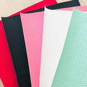 May include: A fan of colorful textured faux leather sheets in red, black, pink, white, and mint green. The sheets have a woven pattern and are fanned out, showcasing the variety of colors and textures.