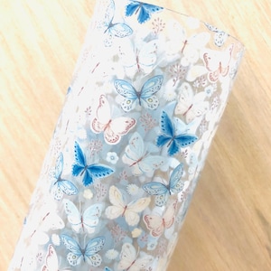 May include: A clear glass tumbler with a blue and white butterfly pattern. The butterflies are scattered across the surface of the glass.