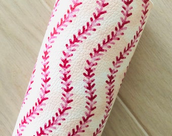 May include: A close-up of a white faux leather sheet with a pink baseball stitch pattern. The sheet is rolled up and the stitching is visible.
