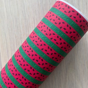 May include: A close-up of a red and green fabric with a watermelon pattern. The fabric has a textured surface and is rolled up.