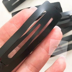 May include: A collection of matte black hair barrettes. Each barrette is rectangular with rounded edges and three rectangular cutouts. The barrettes are made of metal and are designed to hold hair in place.