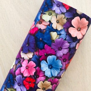 May include: A close-up of a fabric with a floral print. The fabric features a variety of flowers in shades of pink, purple, blue, and beige. The flowers are arranged in a random pattern and appear to be overlapping.