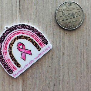 May include: Pink and brown leopard print rainbow with a pink ribbon in the center. The rainbow has the text "breast cancer awareness" written on it.