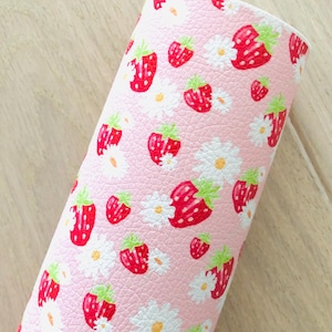 May include: A roll of pink faux leather fabric with a repeating pattern of red strawberries and white daisies. The strawberries have green stems and leaves. The fabric has a textured surface.