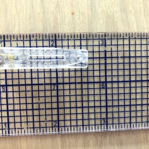 May include: A clear plastic hair clip with a metal spring. The clip is about 2 inches long and is measured against a ruler.