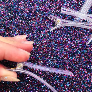 May include: Clear plastic hair clips on a sparkly blue, red, and black background. The clips have a gold metal spring.